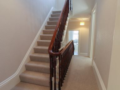 A stairway with wooden banisters and carpet leading to a hallway with doors at Spinnaker House in Scarborough