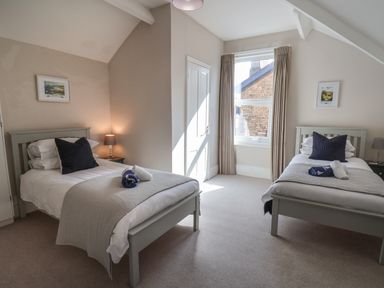 A bedroom with two single beds with pillows and folded towels a window with curtains and nightstands with lamps at Spinnaker House in Scarborough