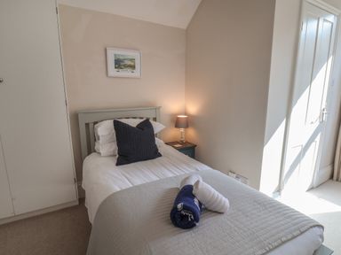 A bedroom with a single bed with pillows and rolled towels beside a nightstand with a lamp at Spinnaker House in Scarborough