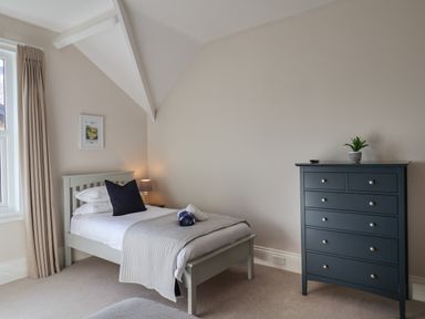 A bedroom with a single bed a bedside table with a lamp a blue chest of drawers and a window with curtains at Spinnaker House in Scarborough