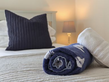 A bed with a large navy pillow and rolled towels on top with a lamp in the background at Spinnaker House in Scarborough