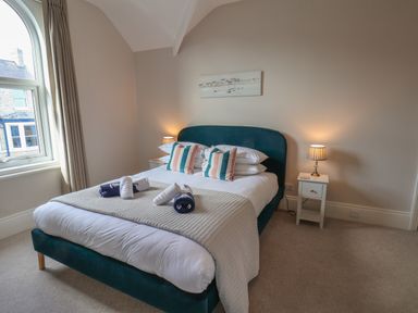 A bedroom with a double bed pillows and rolled towels bedside tables with lamps and a window at Spinnaker House in Scarborough
