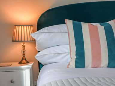 A bed with white pillows and a striped cushion next to a bedside table with a lamp at Spinnaker House in Scarborough
