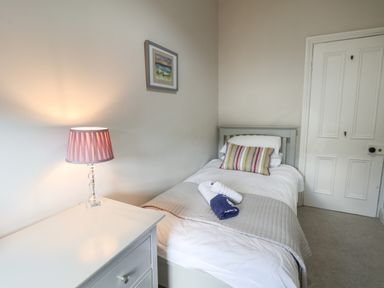A bedroom with a single bed a bedside table with lamp and a wall painting at Spinnaker House in Scarborough