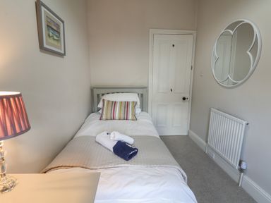 A bedroom with a single bed a side table with a lamp a framed picture a circular mirror and a radiator at Spinnaker House in Scarborough