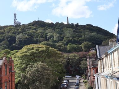 A street with parked cars and houses with a wooded hill and a tall obelisk in the background at Spinnaker House in Scarborough