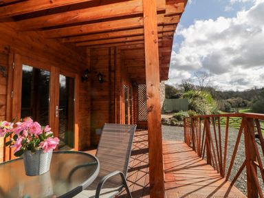 A wooden porch with a glass table and chair overlooking a garden at Bearscombe View in Modbury