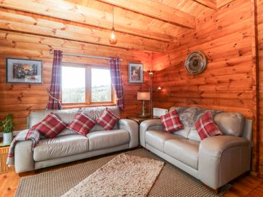 A living room with two gray sofas with red plaid cushions and curtains at Bearscombe View in Modbury