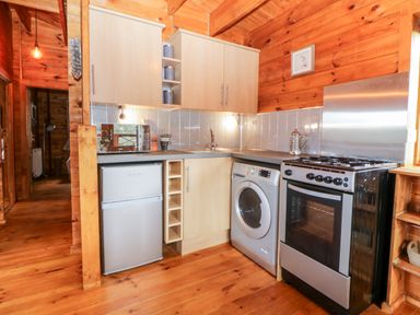 A kitchen with wooden walls and ceiling a refrigerator washing machine oven and cabinets at Bearscombe View in Modbury