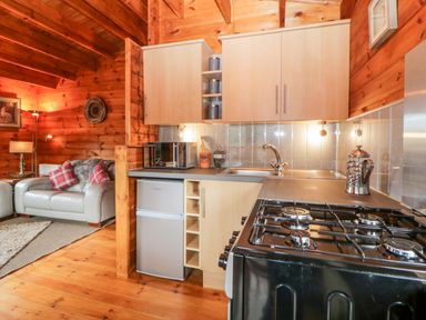 A kitchen area with stove microwave and sink next to a living room with armchair and floor lamps at Bearscombe View in Modbury