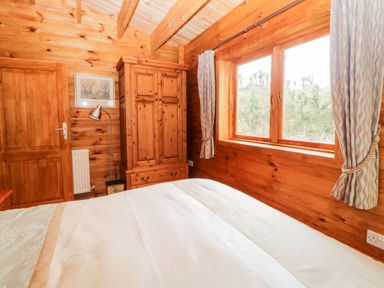 A bedroom with a wooden wardrobe wooden walls and ceiling a bed window with curtains and a floor lamp at Bearscombe View in Modbury