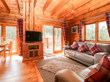 A living room with leather sofas plaid cushions wooden furniture and large windows at Bearscombe View in Modbury