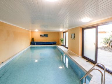 An indoor swimming pool with tiled walls and floor and glass doors leading outside at Bearscombe View in Modbury
