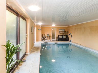 An indoor swimming pool with chairs a table a sofa and plants at Bearscombe View in Modbury