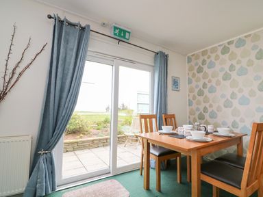 A dining area with a wooden table set with bowls and cups near glass sliding doors at Fairway Lodge in Bigbury-On-Sea