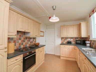 A kitchen with light wood cabinets tiled backsplash oven stovetop microwave toaster and sink at Fairway Lodge in Bigbury-On-Sea