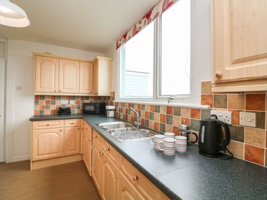 A kitchen with wooden cabinets a countertop with mugs a kettle a microwave and a sink at Fairway Lodge in Bigbury-On-Sea