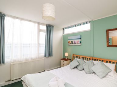 A bedroom with a double bed with pillows bedside table with lamp and window with curtains at Fairway Lodge in Bigbury-On-Sea