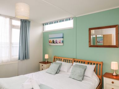 A bedroom with a double bed two bedside tables with lamps a wooden framed mirror and a window with blue curtains at Fairway Lodge in Bigbury-On-Sea