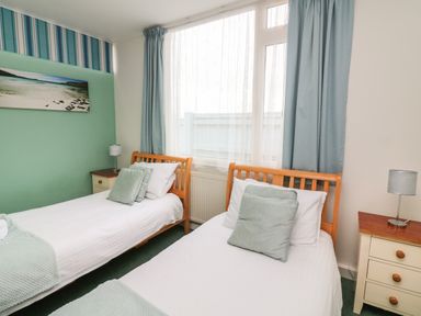 A bedroom with two single beds side by side with wooden frames bedside tables with lamps and a window with curtains at Fairway Lodge in Bigbury-On-Sea