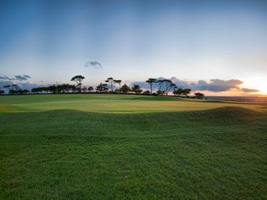 A golf course green with a flag and trees in the background at Fairway Lodge in Bigbury-On-Sea