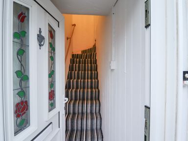 A narrow staircase with striped carpet leading up from a white hallway with a door featuring stained glass panels at Monteva Whitby