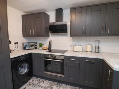 A kitchen with dark cabinets a washing machine oven stovetop toaster kettle and microwave at Monteva Whitby