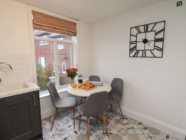 A dining area with a round table four gray chairs a large clock on the wall and a window showing a neighboring house at Monteva in Whitby
