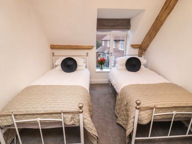A bedroom with two single beds with beige quilts and circular pillows by a window with flowers at Monteva Whitby