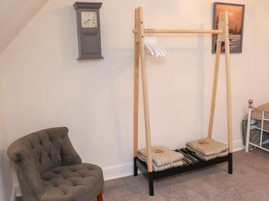A small corner of a bedroom with a gray upholstered chair a wooden clothes rack with hangers and folded blankets a wall clock and a framed picture at Monteva Whitby