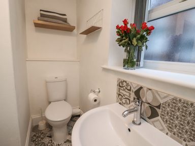A bathroom with a toilet a sink with a faucet a toilet brush a roll of toilet paper red flowers in a vase on the window sill and patterned tiles behind the sink at Monteva Whitby