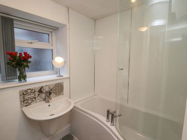A bathroom with a sink a bathtub with glass screen a window with blinds and a vase of red flowers at Monteva in Whitby