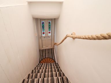 A staircase with striped carpet leading down to a door with stained glass panels and a rope handrail at Monteva Whitby