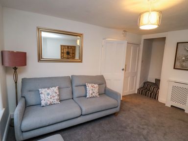 A living room with a grey sofa two floral cushions a floor lamp a mirror and a staircase at Monteva in Whitby