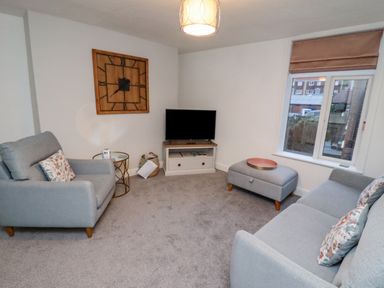 A living room with a sofa armchair ottoman television and wall clock at Monteva in Whitby