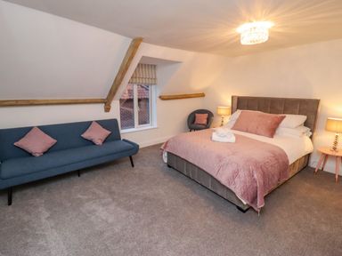 A bedroom with a bed with pink bedding a blue sofa two lamps and a window at Monteva in Whitby