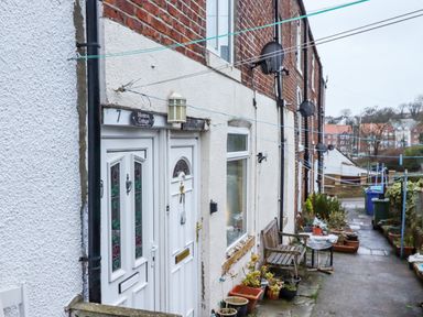 A row of cottages with white doors and potted plants outside along a narrow pathway at Monteva in Whitby