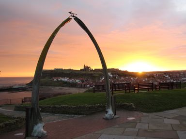 A whale bone arch with benches and a view of the town and coastline at sunset at Monteva in Whitby