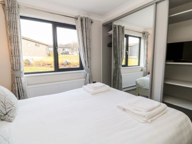 A bedroom with a bed, folded towels, a window with curtains, and a mirrored wardrobe at Mayflower Broadwoodwidger near Ashwater
