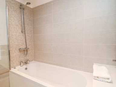 A bathroom with a bathtub shower combination and folded towels on the counter at Mayflower Broadwoodwidger near Ashwater