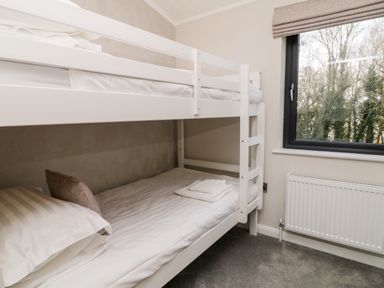 A bedroom with white bunk beds towels and pillows next to a window and radiator at Mayflower Broadwoodwidger near Ashwater