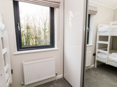 A bedroom with white bunk beds a window with a gray frame a radiator and a mirrored wardrobe at Mayflower Broadwoodwidger near Ashwater