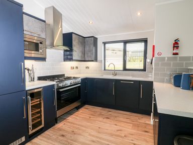 A kitchen with blue cabinets a gas stove a microwave a wine cooler a window with blinds and wooden floor at Mayflower Broadwoodwidger near Ashwater