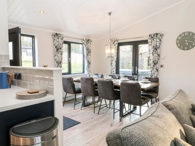 A dining area with a table set for six next to windows and doors with curtains at Mayflower in Broadwoodwidger near Ashwater