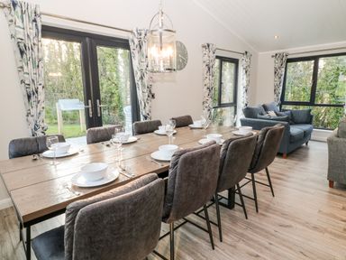 A dining area with set table and chairs next to a sitting area with sofas and windows at Mayflower in Broadwoodwidger near Ashwater