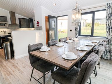 A dining area with a wooden table set for eight and an open door to a kitchen at Mayflower Broadwoodwidger near Ashwater