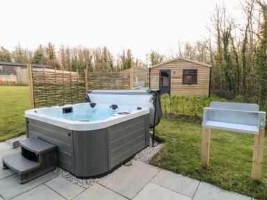 An outdoor hot tub with steps a wooden shed and a metal barbecue grill on a grassy lawn at Mayflower in Broadwoodwidger near Ashwater