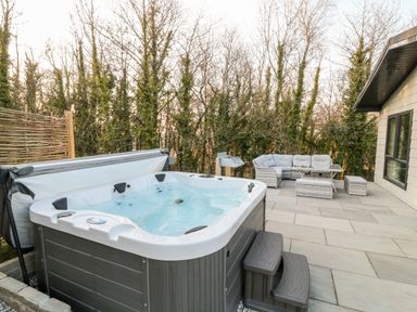 An outdoor patio with a hot tub and a seating area with a sofa and table at Mayflower in Broadwoodwidger near Ashwater