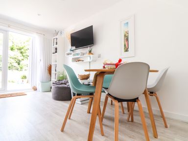 A dining area with a wooden table and chairs next to a wall-mounted TV and bookshelf in a room at Penpoll Little Petherick Creek near Padstow
