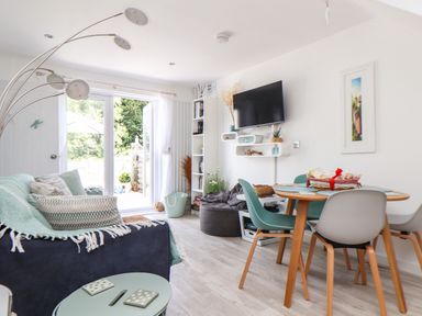 A living room with a sofa dining table chairs and a wall-mounted television at Penpoll Little Petherick Creek near Padstow